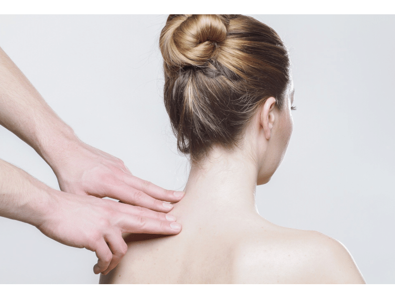 „Farbbild einer Frau von hinten, während Hände sanft auf ihr Schulterblatt zeigen, um eine beruhigende und entspannende Massage darzustellen.“